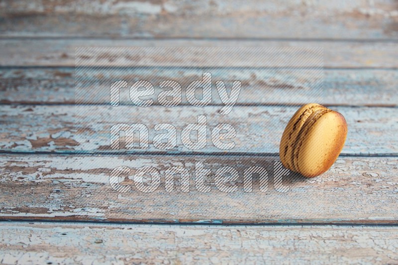 45º Shot of Yellow Crème Brulée macaron on light blue wooden background