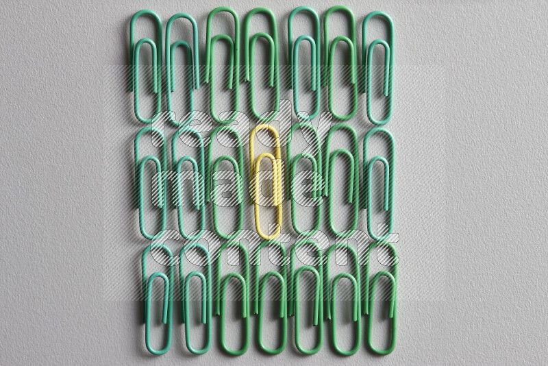 مجموعة من مشابك الورق الخضراء مع مشبك ورق ملون مختلف في المنتصف على خلفية رمادية