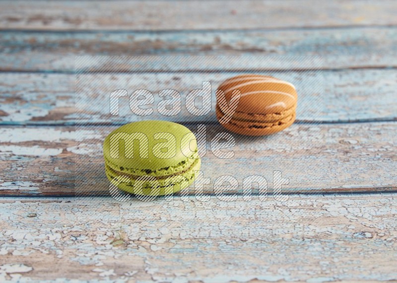 45º Shot of of two assorted Brown Irish Cream, and Green Pistachio macarons  on light blue background