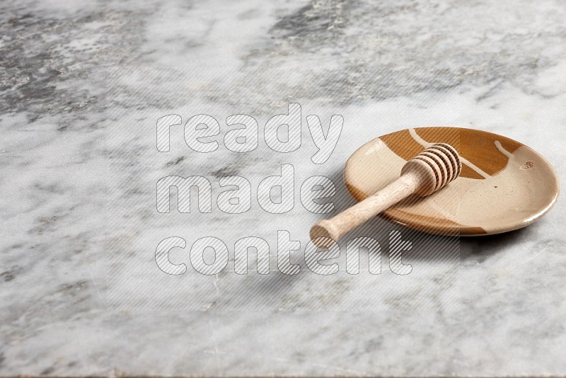 Multicolored Pottery Plate with wooden honey handle in it, on grey marble flooring, 45 degree angle