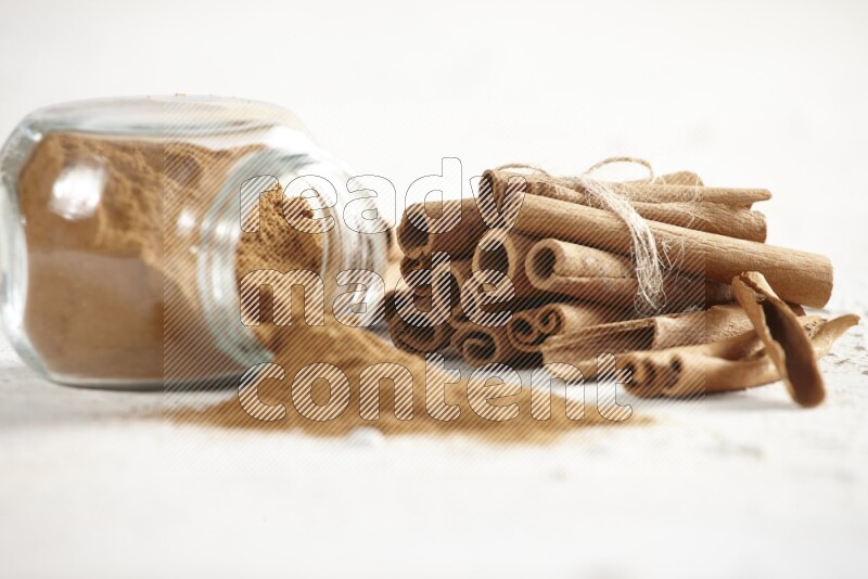 Flipped herbs glass jar full of cinnamon powder and cinnamon sticks in the back on a textured white background