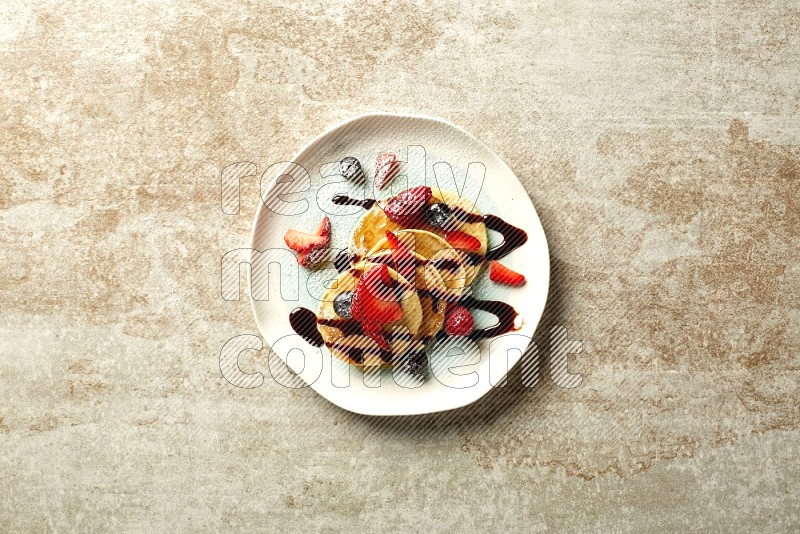 Five stacked mixed berries mini pancakes in a bicolor plate on beige background