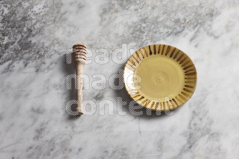 Multicolored pottery plate with wooden honey dipper on the side on grey marble background
