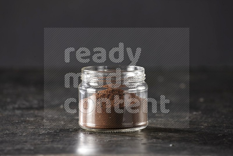 A glass jar full of cloves powder on a textured black flooring