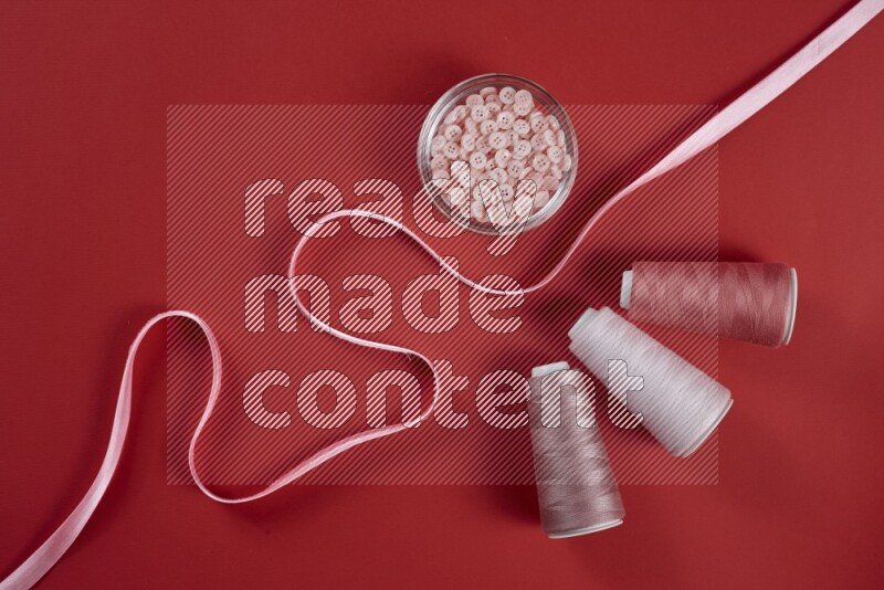 A pink and red collection of sewing and tailoring tools arranged on a red background