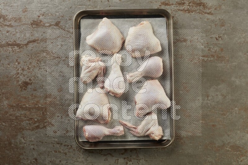 Mixed fresh chicken pieces in an oven tray on a textured rustic background