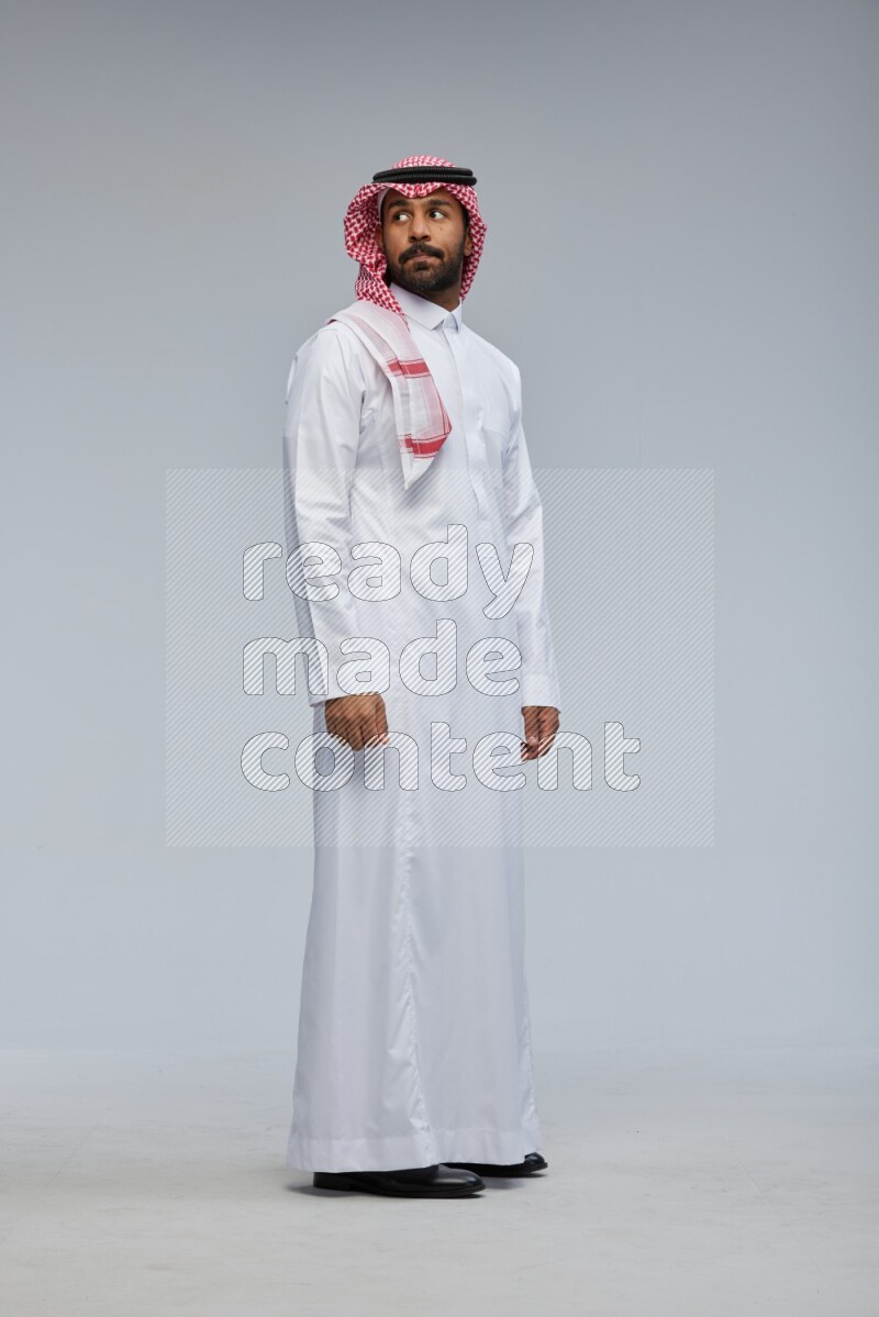 Saudi man Wearing Thob and shomag standing interacting with the camera on Gray background