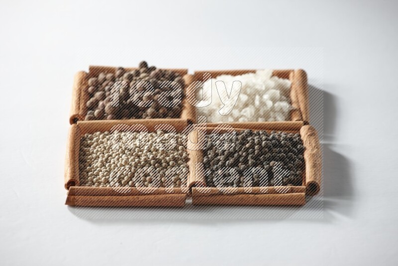4 squares of cinnamon sticks full of allspice, white salt, white pepper and black pepper on white flooring