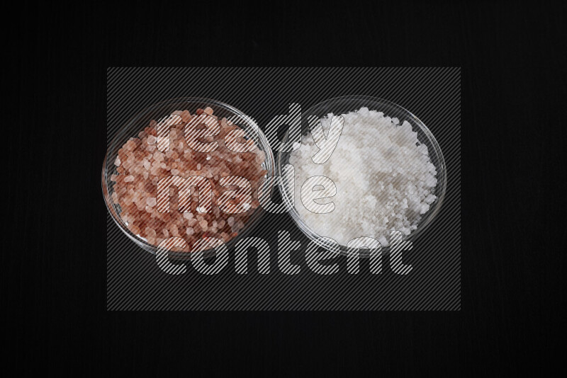 2 glass bowls one is filled with himalayan salt and the other with white salt on black background