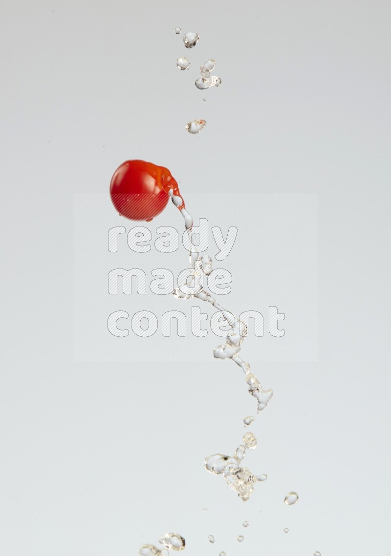 A single cherry tomato flying leaving a splash of water behind on a light blue background