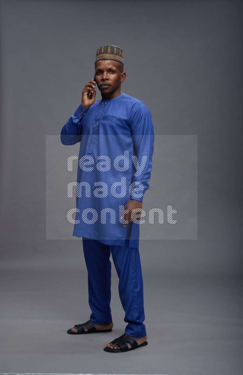 Man wearing Nigerian outfit standing talking on phone on gray background