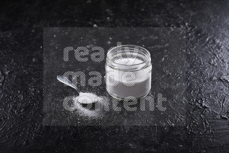 A glass jar full of fine table salt on black background