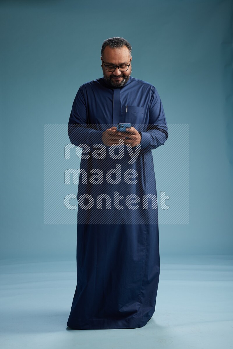 Saudi Man without shimag Standing texting on phone on blue background