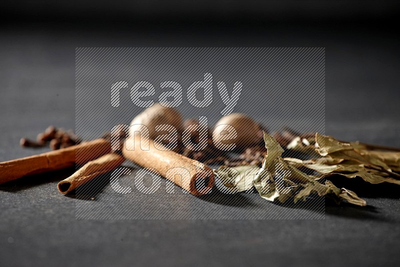 Cloves, ginger, bay laurel and cinnamon sticks on black flooring