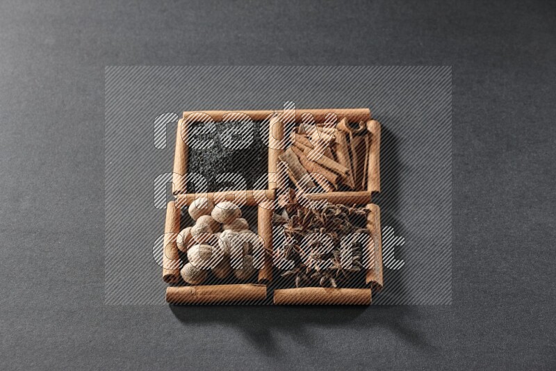 4 مربعات من عيدان القرفة ممتلئة بحبة البركة السوداء والقرفة واليانسون النجمي وجوزة الطيب على أرضية سوداء