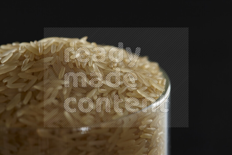 Basmati golden rice in a glass jar on black background