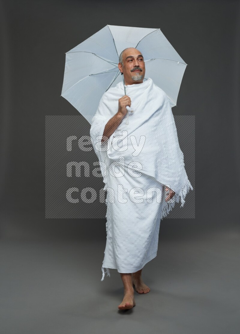 A man wearing Ehram Standing holding umbrella on gray background