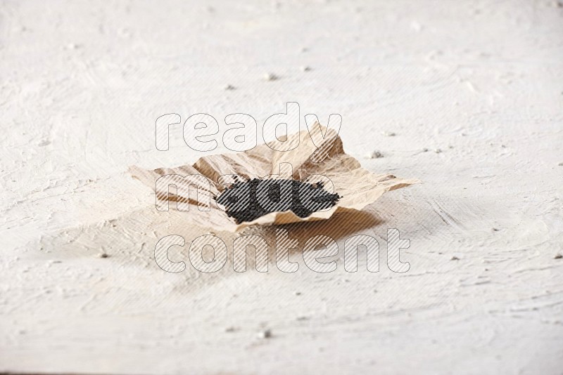 A crumpled piece of paper full of black seeds on a textured white flooring