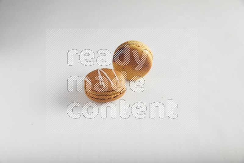 45º Shot of of two assorted Brown Irish Cream, and Yellow Crème Brulée macarons on white background