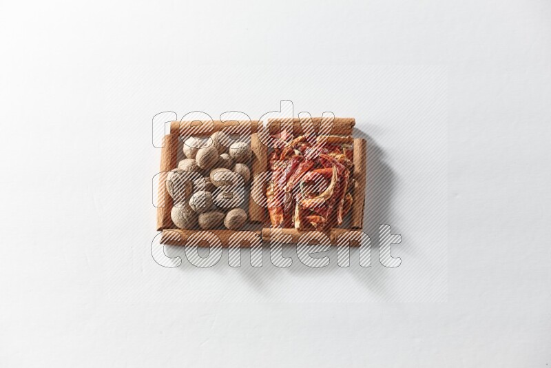 مربعان من أعواد القرفة ممتلئان بالفلفل الحار المجفف وجوزة الطيب علي خلفية بيضاء