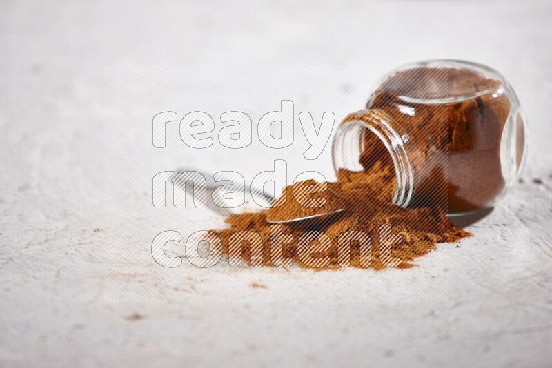 A glass jar full of ground paprika powder flipped with some spilling powder on white background