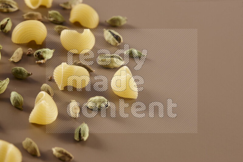 Raw pasta with different ingredients such as cherry tomatoes, garlic, onions, red chilis, black pepper, white pepper, bay laurel leaves, rosemary and cardamom on beige background