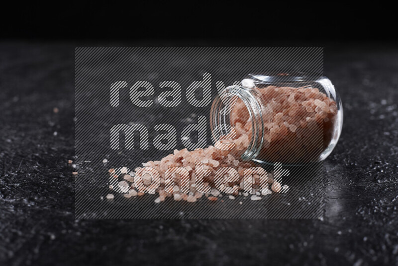 A glass jar full of coarse himalayan salt crystals on black background