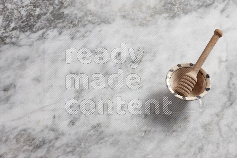 Decorative pottery bowl with wooden honey dipper in it on grey marble background