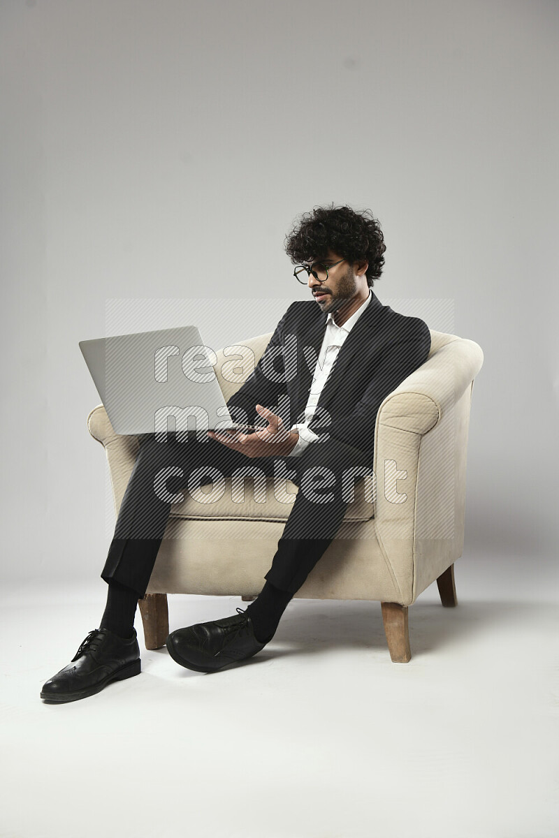 رجل يرتدي ملابس رسمية يجلس علي كرسي و يعمل علي لاب توب علي خلفية بيضاء