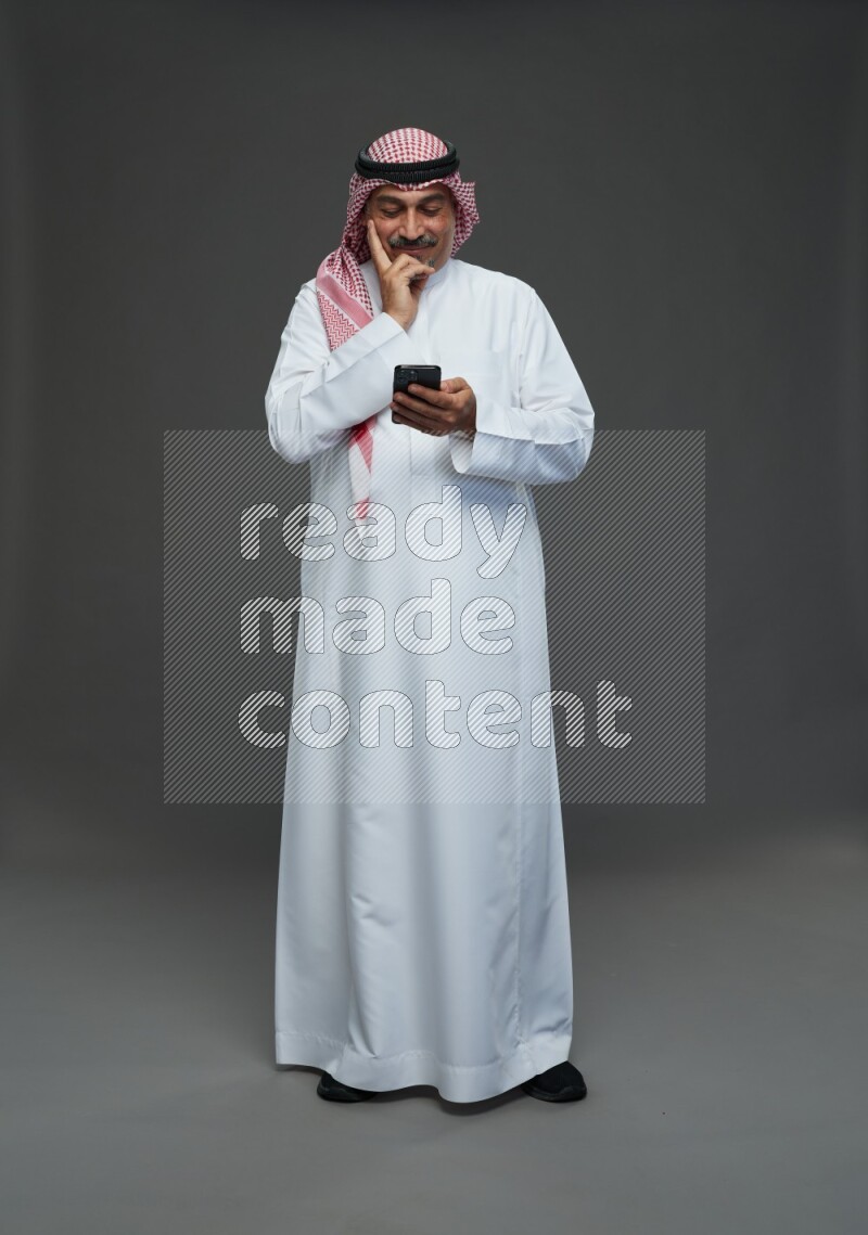 Saudi man with shomag Standing texting on phone on gray background