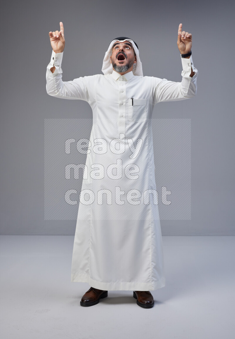 Saudi man Wearing Thob and white Shomag standing interacting with the camera on Gray background