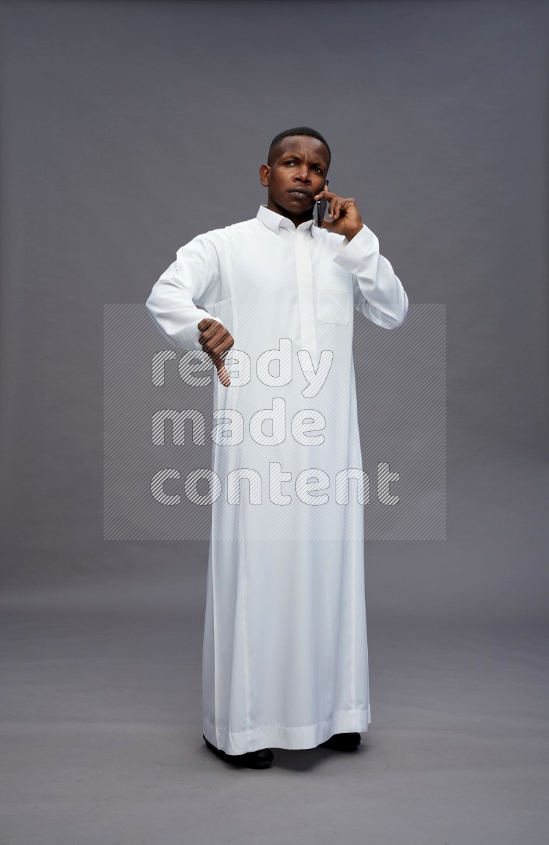 Saudi man wearing thob standing talking on phone on gray background