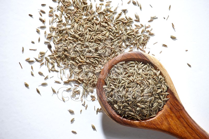 A wooden ladle full of cumin seeds on a white flooring