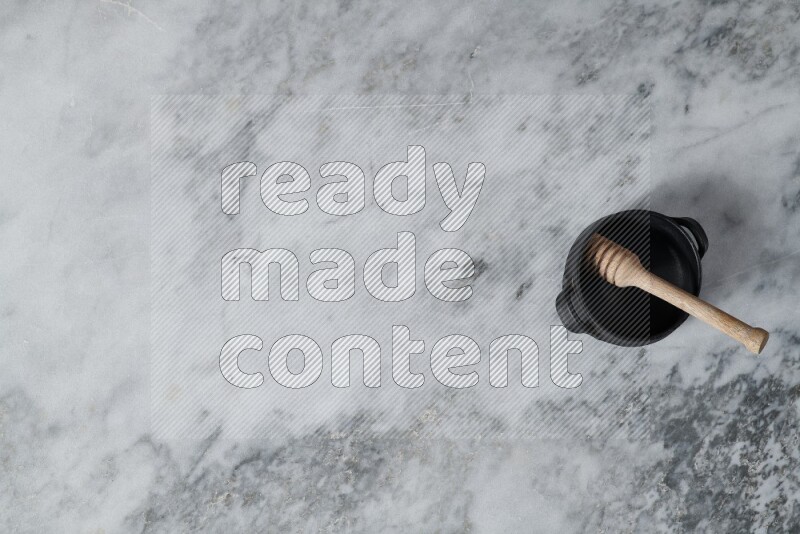 Black pottery bowl with wooden honey dipper in it on grey marble background
