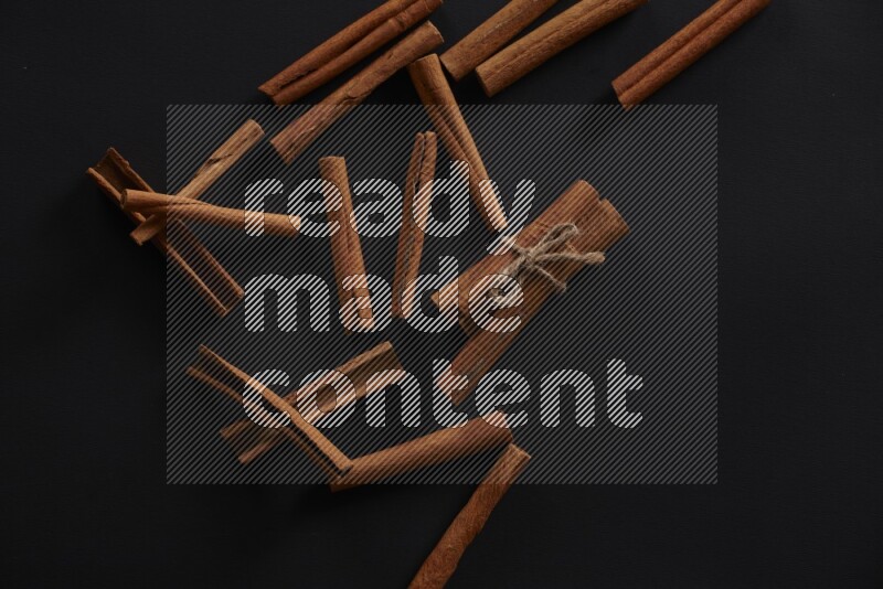 4 Cinnamon sticks stacked and bounded with more sticks in the background on black flooring