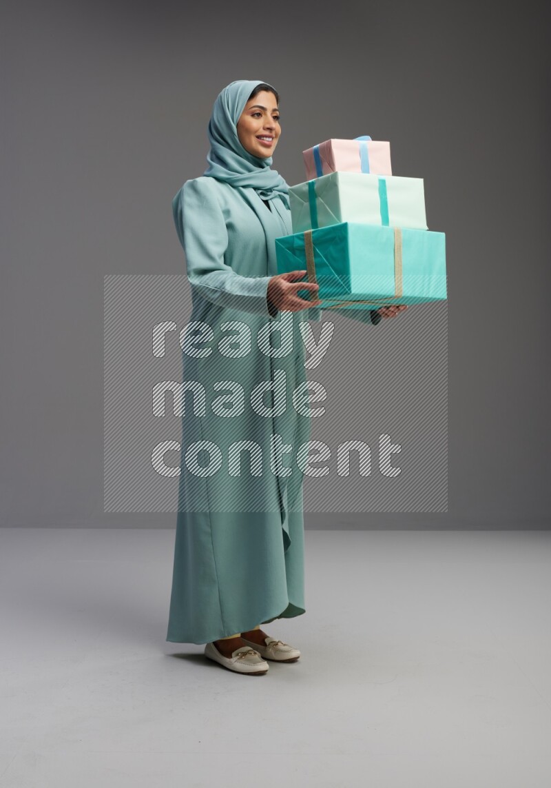 Saudi Woman wearing Abaya standing holding gift box on Gray background
