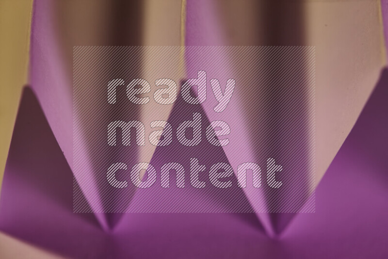 A close-up abstract image showing sharp geometric paper folds in pink gradients and warm tones
