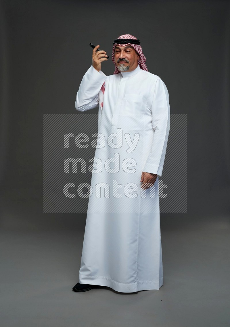 Saudi man with shomag Standing talking on phone on gray background