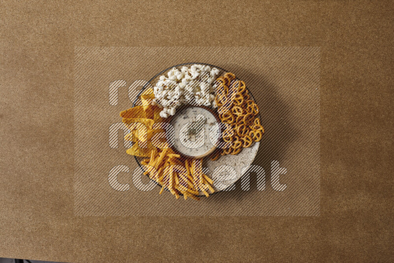 Assorted snacks on a pottery plate with a dipping on brown background