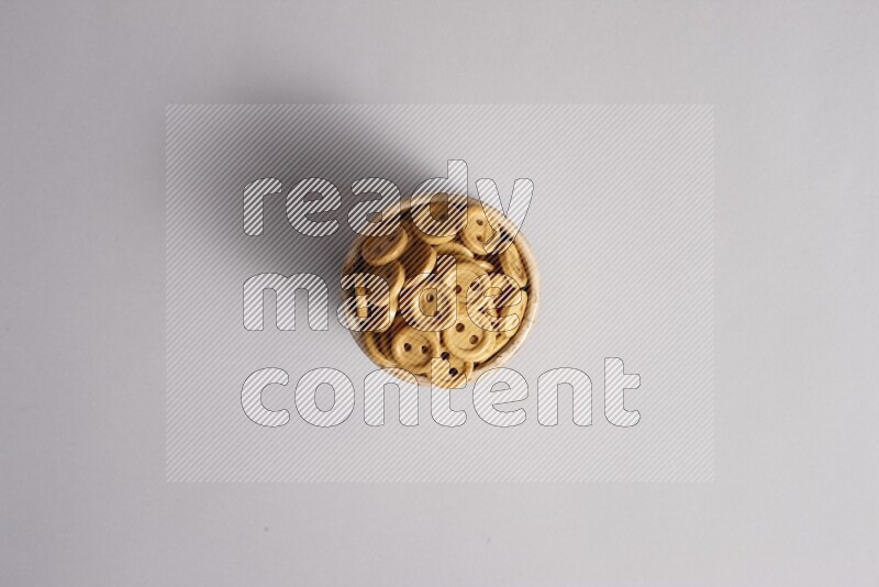 Colored buttons in a beige pottery bowl on grey background