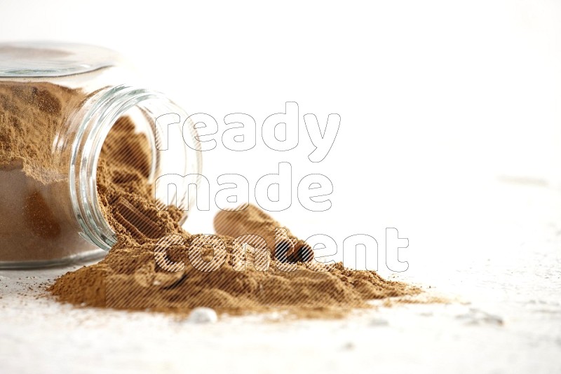 Flipped glass jar full of cinnamon powder with some pieces of cinnamon sticks on a textured white background