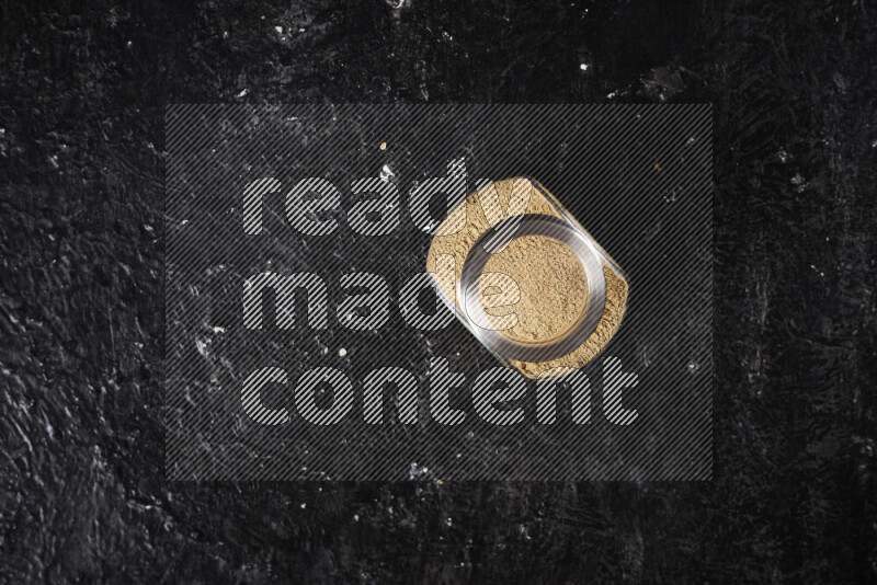 A glass jar full of ground ginger powder on black background