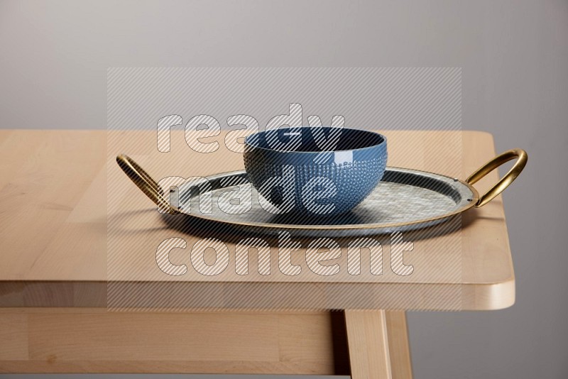 blue bowl placed on a rounded stainless steel metal tray with golden handels on the edge of wooden table