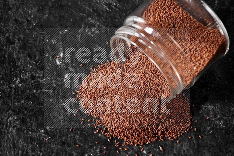 A glass jar full of garden cress seeds flipped and seeds spread out on a textured black flooring