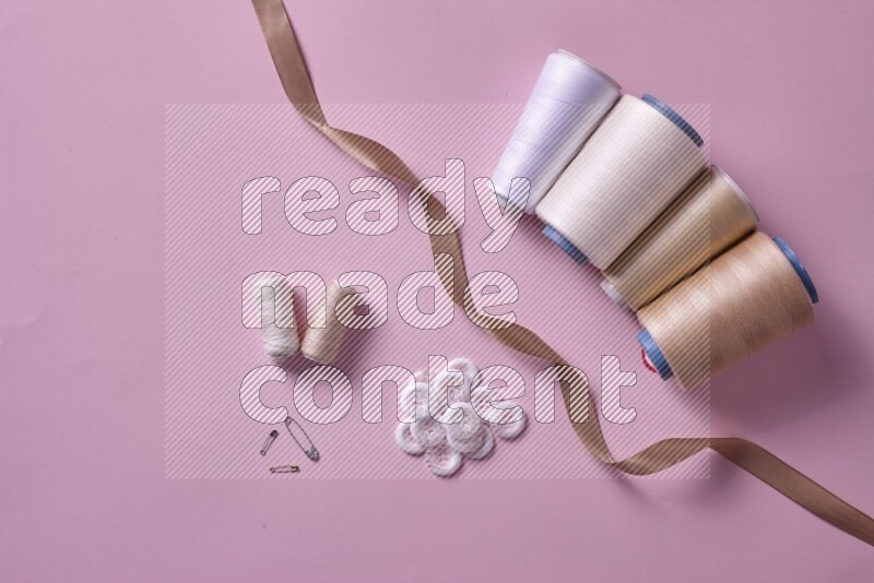 A white and pink collection of sewing and tailoring tools arranged on a pink background