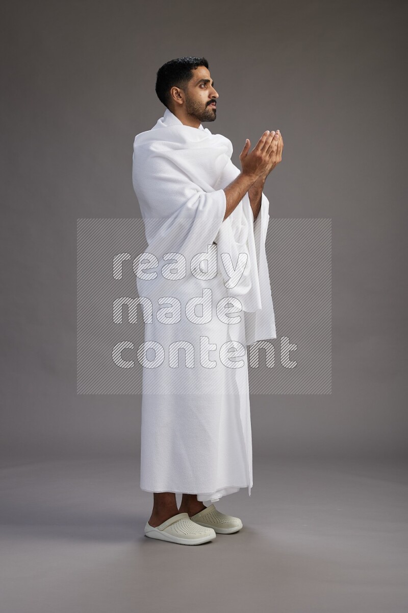 A man wearing Ehram Standing performing dua'a on gray background