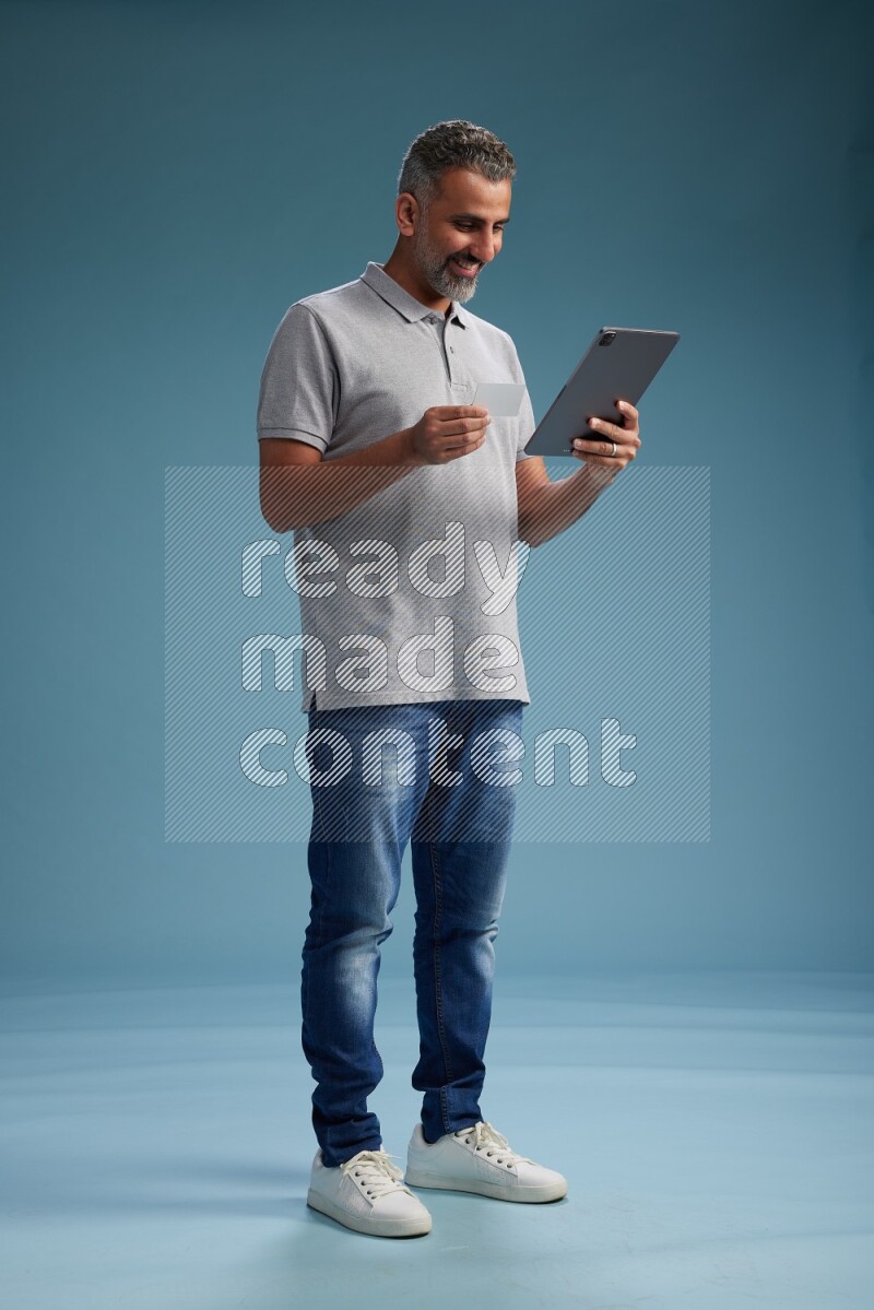 Man Standing holding ATM while working on tablet on blue background