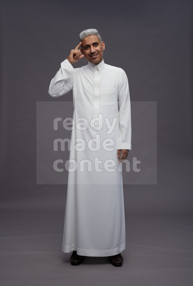 Saudi man wearing thob standing interacting with the camera on gray background