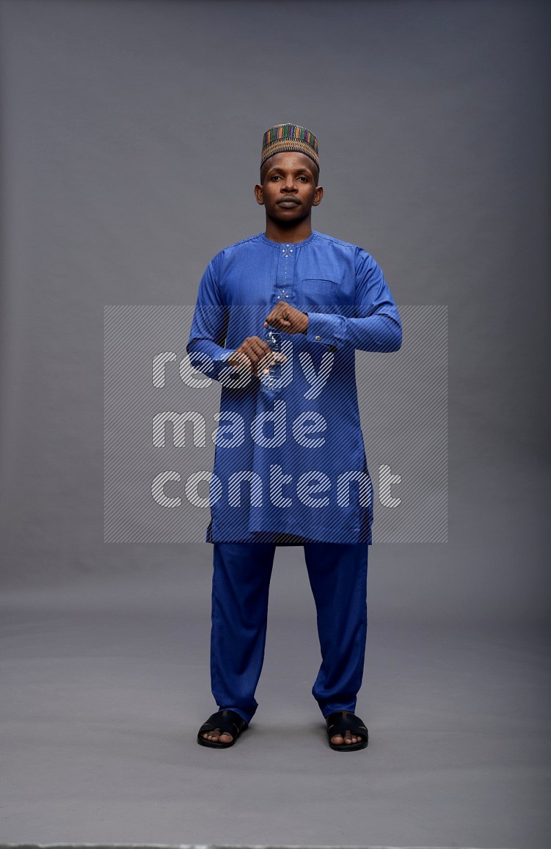 Man wearing Nigerian outfit standing drinking water on gray background