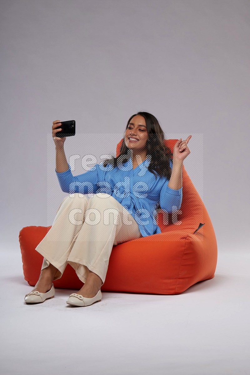 A woman sitting on an orange beanbag and taking selfie